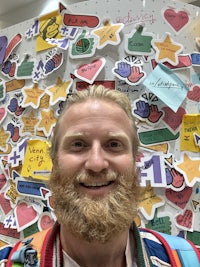 a man with a beard standing in front of a wall full of stickers