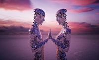 two metal figures standing in the desert with a sunset behind them